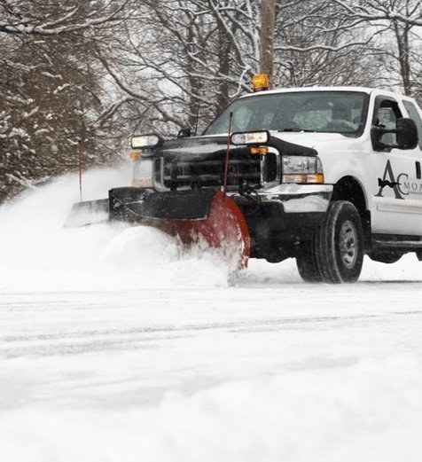 AC Moate Industries snow plow truck clearing commercial parking lot in winter